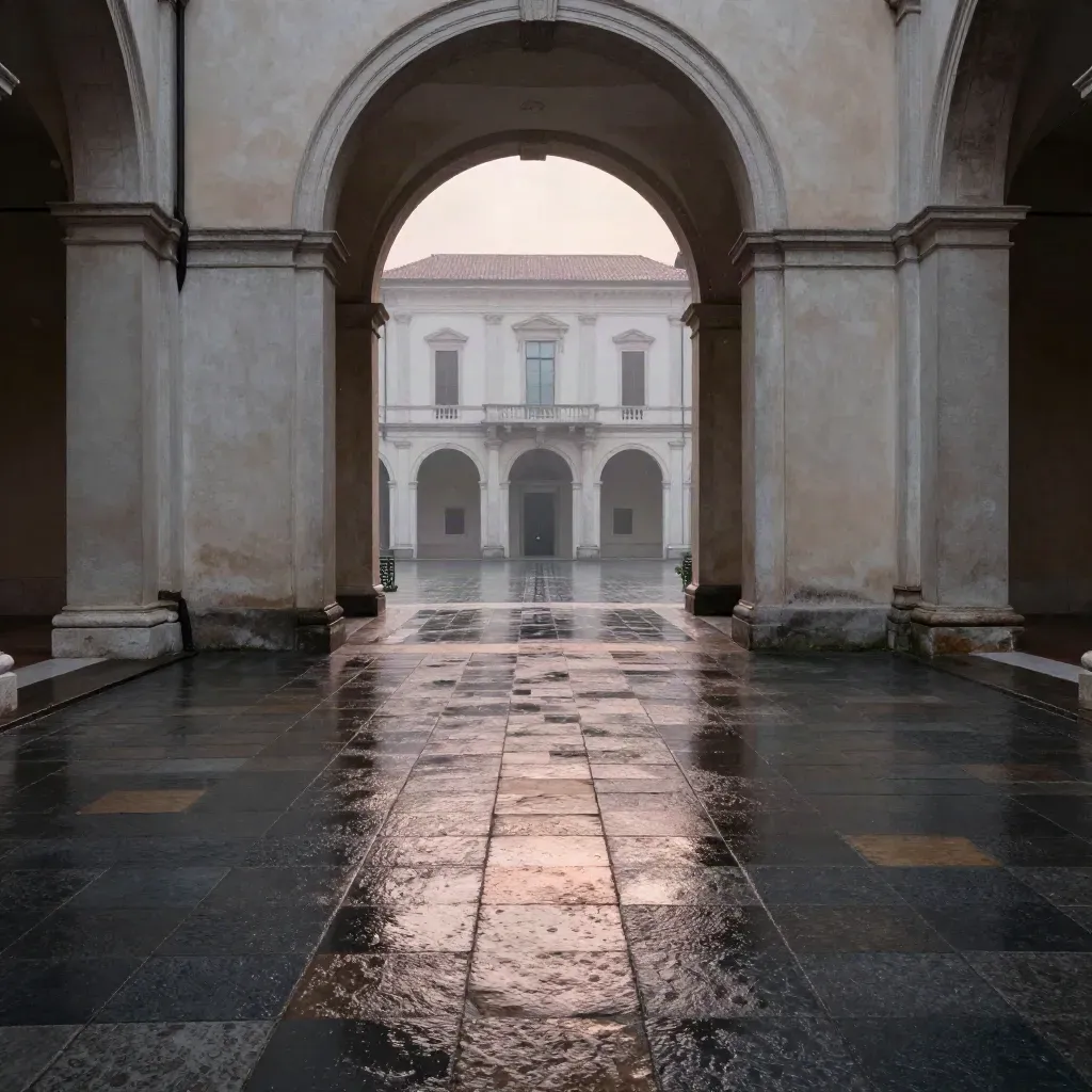 Corte in pietra lombarda bagnata dalla pioggia, arco alto e facciata lontana.